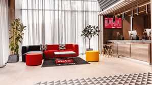 Un moderno vestíbulo de hotel con un sofá rojo, un reposapiés amarillo y un mostrador de recepción.