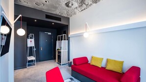 Una sala moderna con un sofá rojo, una butaca roja y una mesita. Se ve una escalera con un bolso blanco y una puerta al fondo.