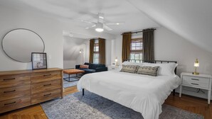 A bedroom with a large bed, a wooden dresser, a round mirror, a ceiling fan, and a window with curtains. - Renovated Water Haus ⎥ +8 beds ⎥ Historic Waterfront

 (Warren)