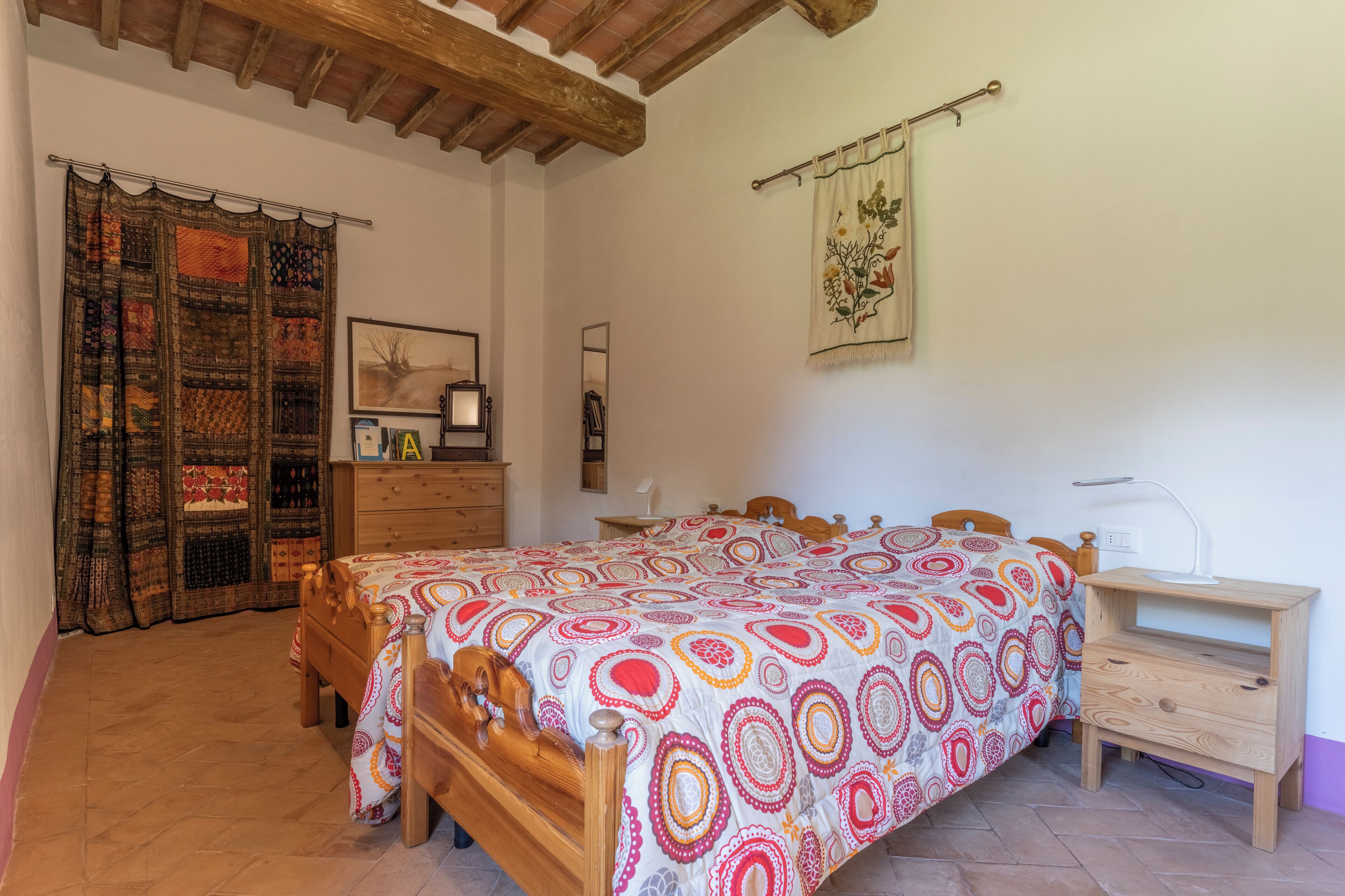 A bedroom with a wooden bed, a nightstand, a dresser, a mirror, and a curtain with a patchwork design.