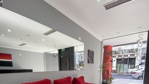 Un canapé rouge dans un hall d’entrée moderne, agrémenté d’un grand miroir, d’une plante en pot et offrant une vue sur la rue.