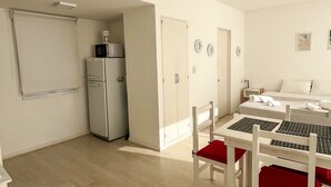 Une pièce de taille modeste comprenant un coin cuisine, un lit, une table avec des chaises et une fenêtre.