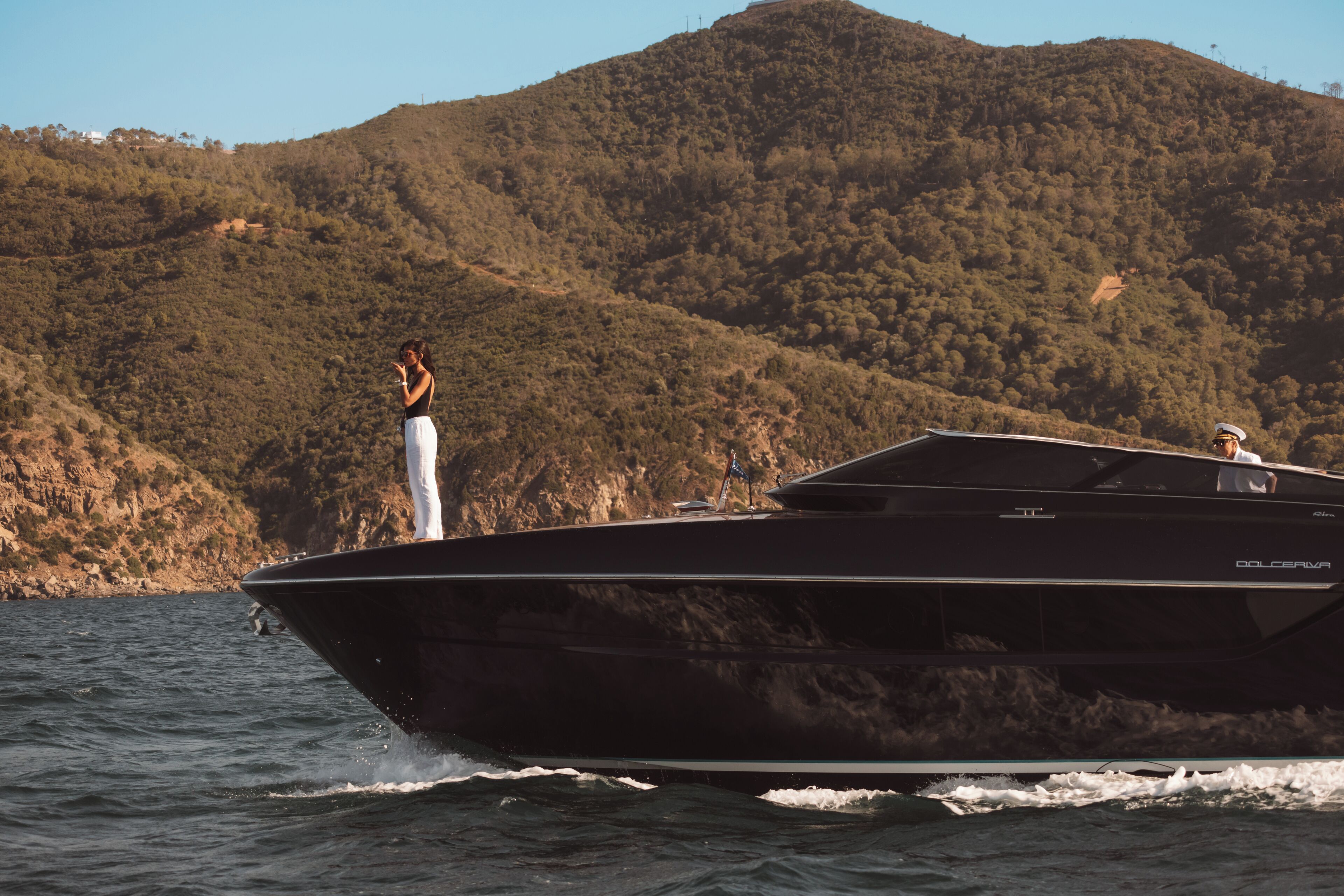 A large, sleek black boat on water with a mountainous backdrop.