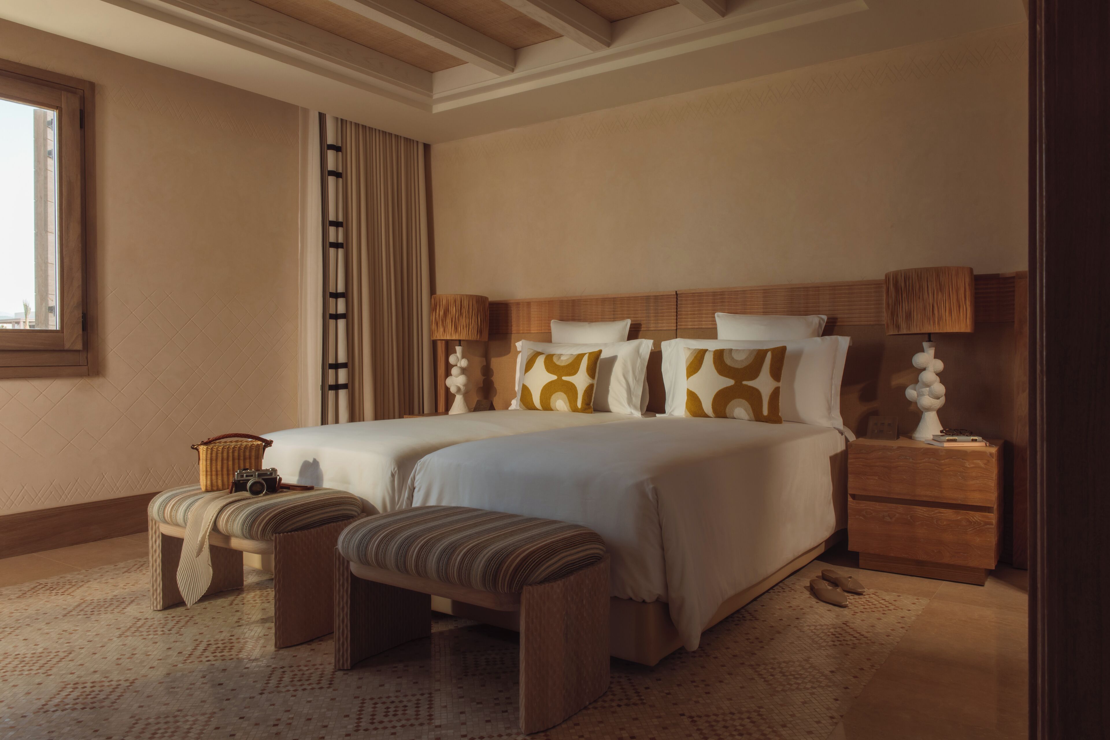 A spacious bedroom with a large bed, two bedside tables, a bench, and a window.