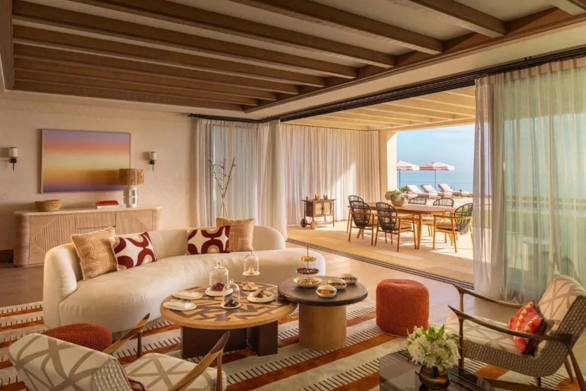 A spacious living area with a large sofa, a coffee table, and a dining set. There is a view of the ocean through large windows.