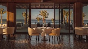 A dining area with a view of the ocean, featuring a round table with chairs and a patterned floor. - Royal Mansour Tamuda Bay (M'diq)