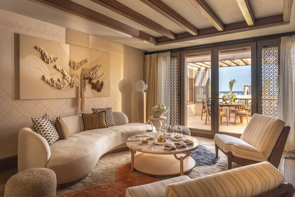 A modern living room with a curved sofa, a round coffee table, and a view of the outdoor patio. - Royal Mansour Tamuda Bay (M'diq)