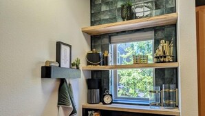 Una cocina con ventanal, estantes con utensilios de cocina y un reloj.