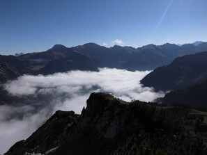Un paisaje montañoso con un valle de nubes y un pico rocoso en primer plano.