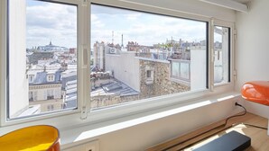 A room with a large window overlooking a cityscape, a desk with a chair, and a power outlet. - Masterpiece loft Eiffel Tower view in enchanting Paris (Paris)