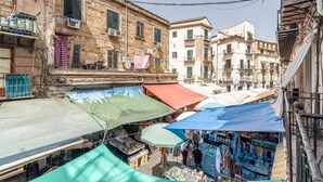 A narrow street with outdoor market stalls under canopies, buildings with balconies, and a clear sky. - La Casa sul Mercato by Wonderful Italy (Palermo)