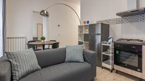 A modern kitchen with a gas stove, oven, and a built-in refrigerator. There is a gray sofa with striped pillows in the living area. - La Casa sul Mercato by Wonderful Italy (Palermo)