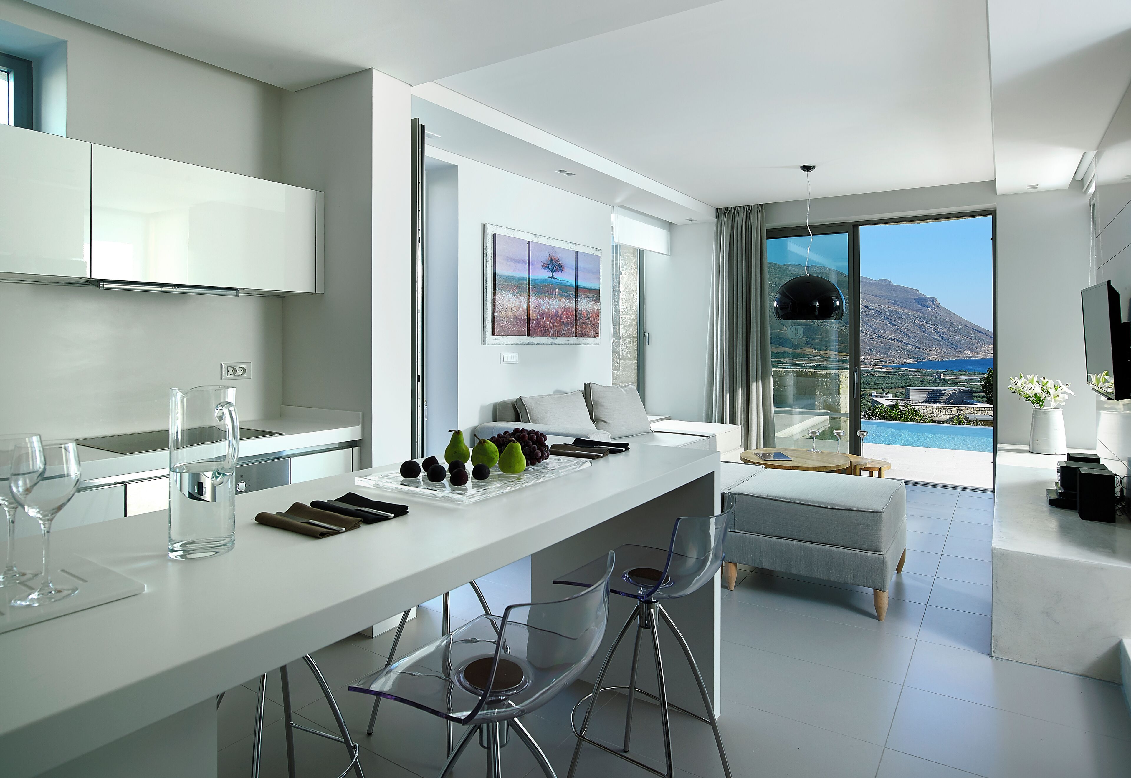 Eine moderne Küche mit einer zentralen Kochinsel, Barhocker und Blick auf eine gebirgige Landschaft durch große Fenster.