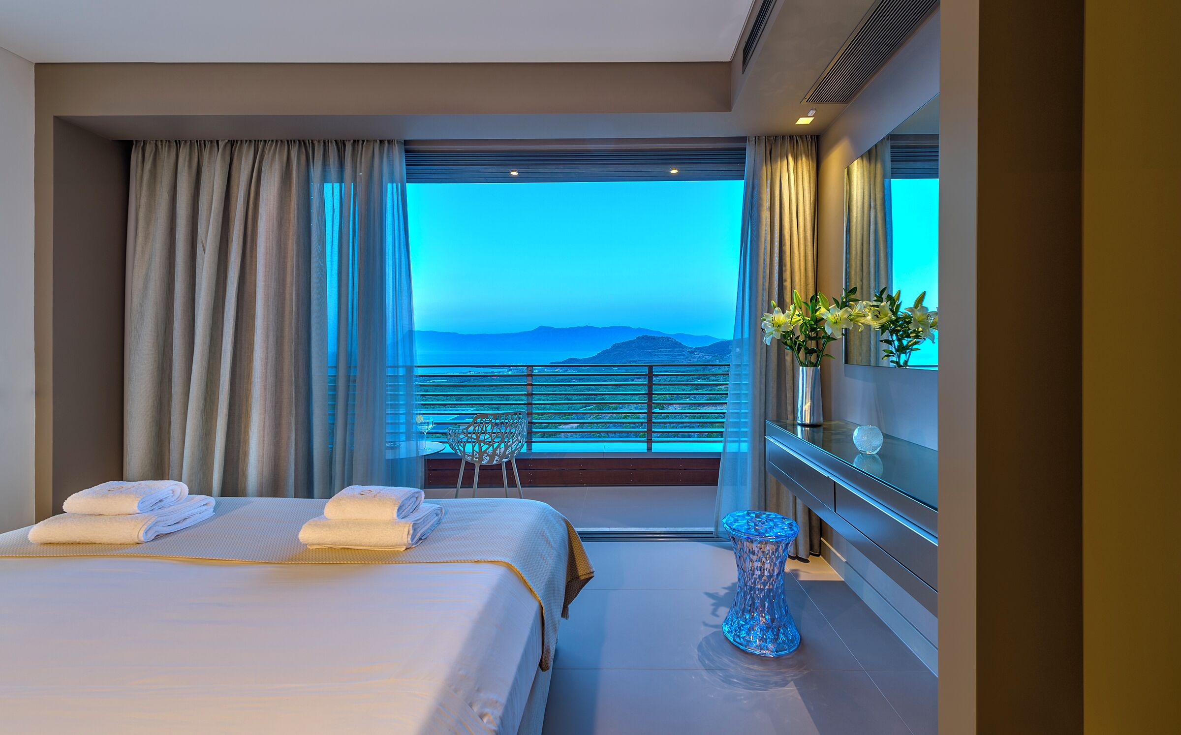 Ein Hotelzimmer mit Bett, Sessel, Blumenvase und Meerblick.