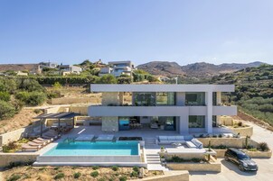 Una casa moderna de dos pisos con piscina, mobiliario exterior y vistas a las colinas circundantes.