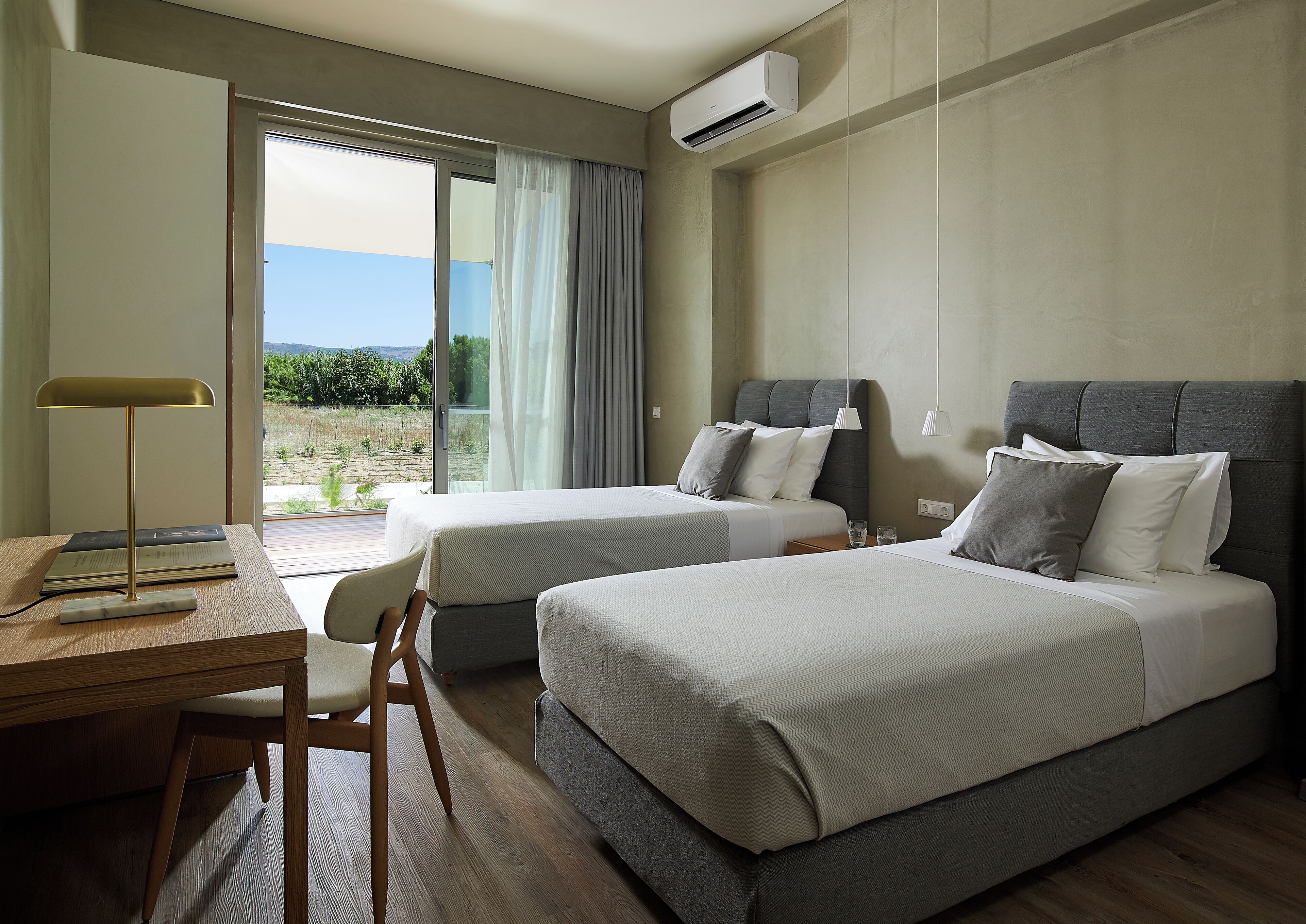 A hotel room with two beds, a desk, a chair, and a view of the outdoors.