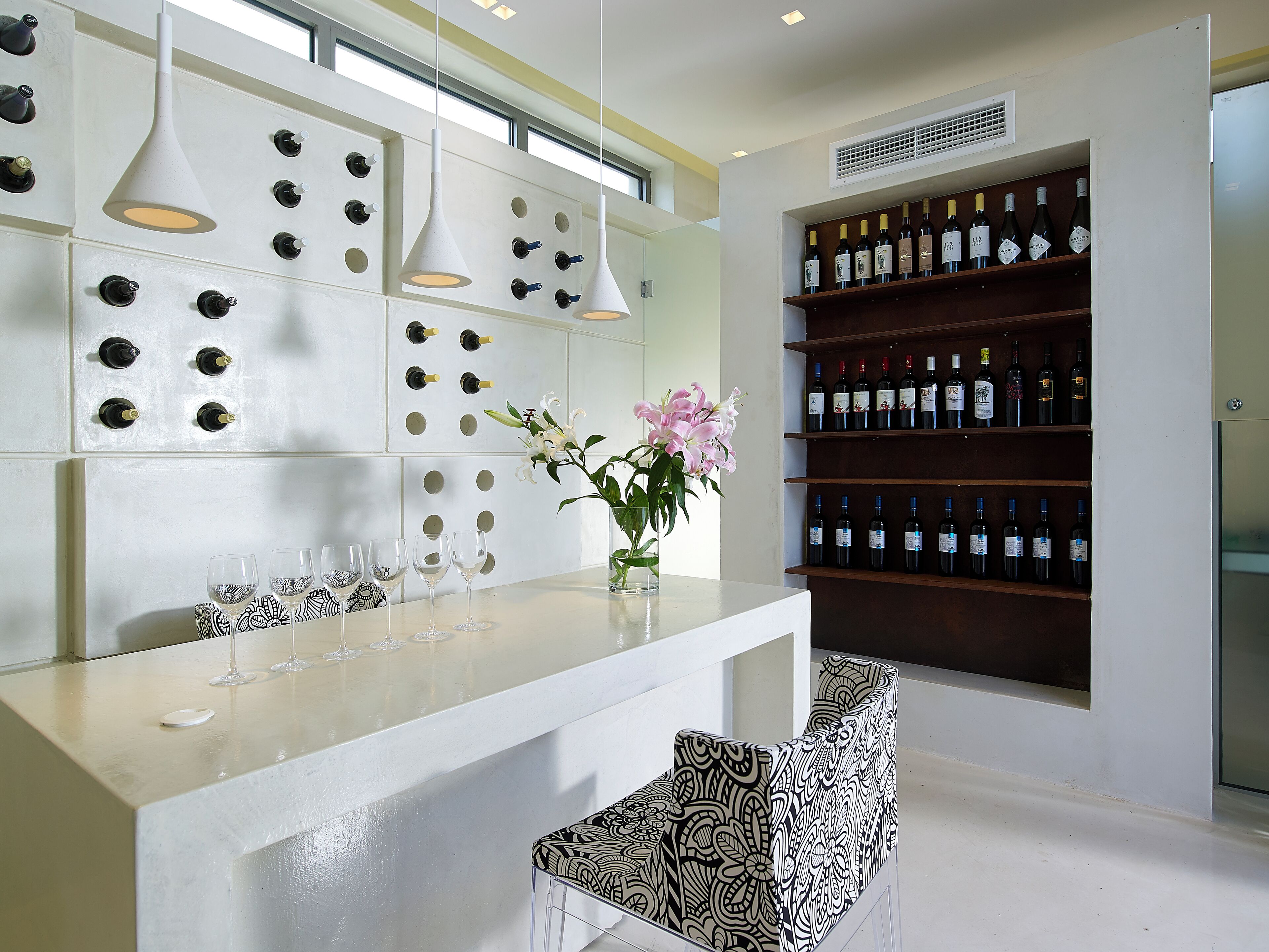 A modern bar area with a wine rack, hanging lights, and a vase with flowers.
