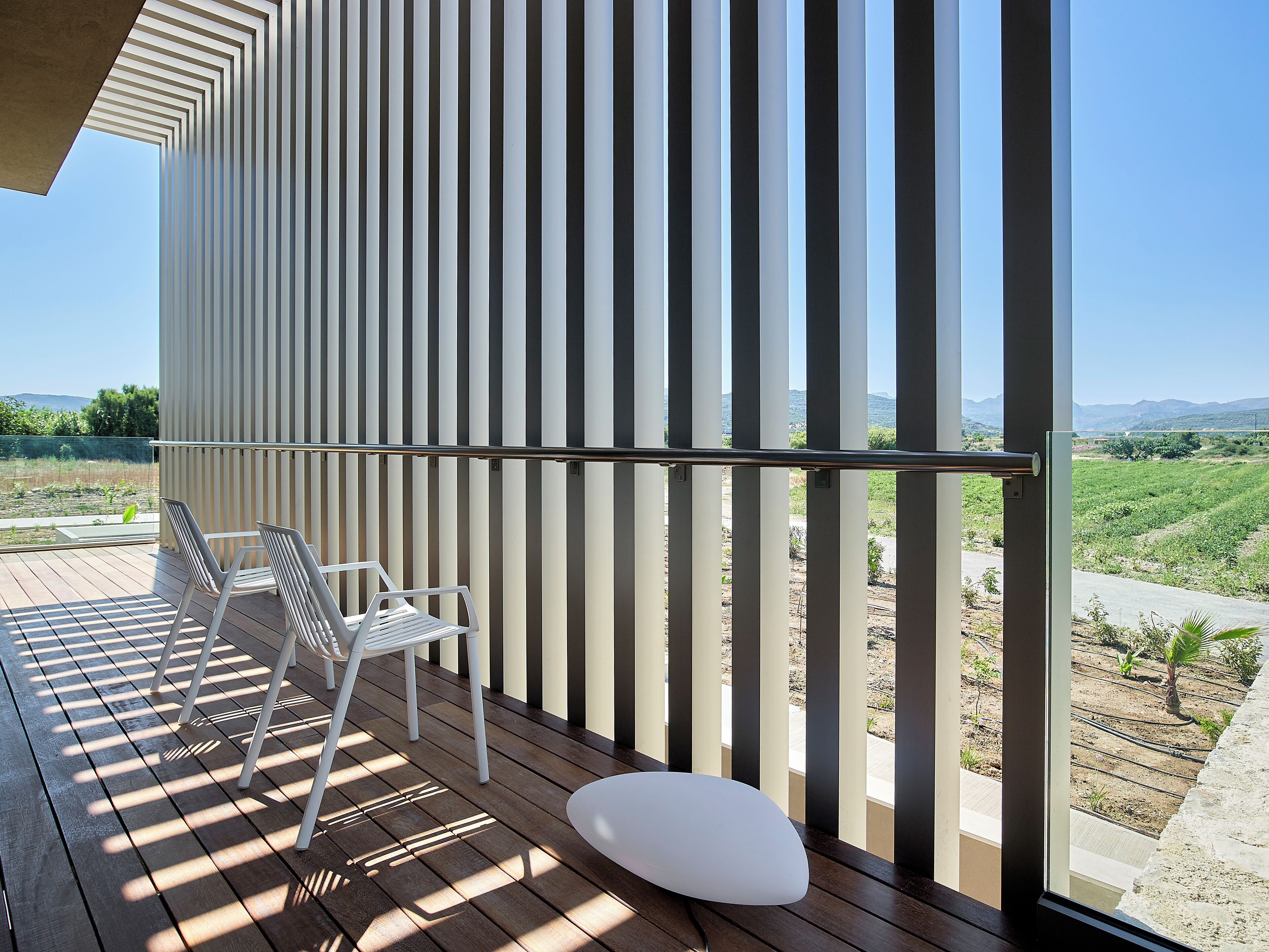 A balcony with a wooden floor, two white chairs, and a white table.