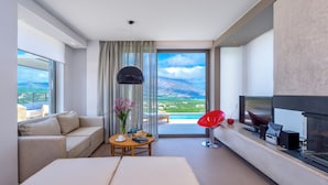 A modern hotel room with a large window, a sofa, a coffee table, a red chair, and a TV.