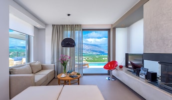 A modern hotel room with a large window, a sofa, a coffee table, a red chair, and a TV.