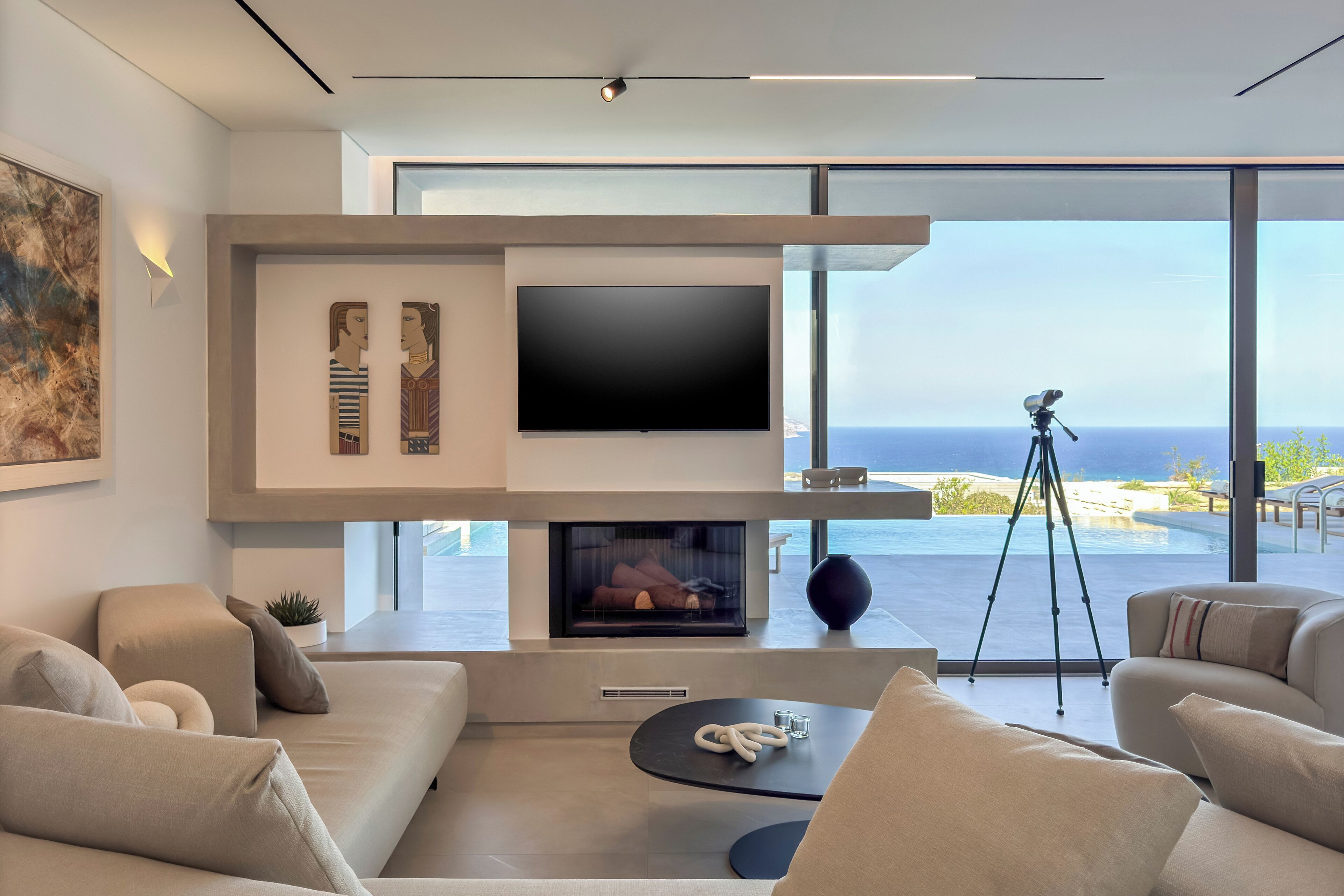 A modern living room with a flat-screen TV, a fireplace, and a large window overlooking the ocean.