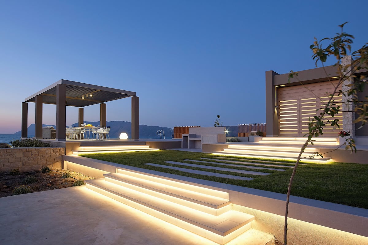 A modern outdoor patio with a pergola, seating area, and steps leading to a building.