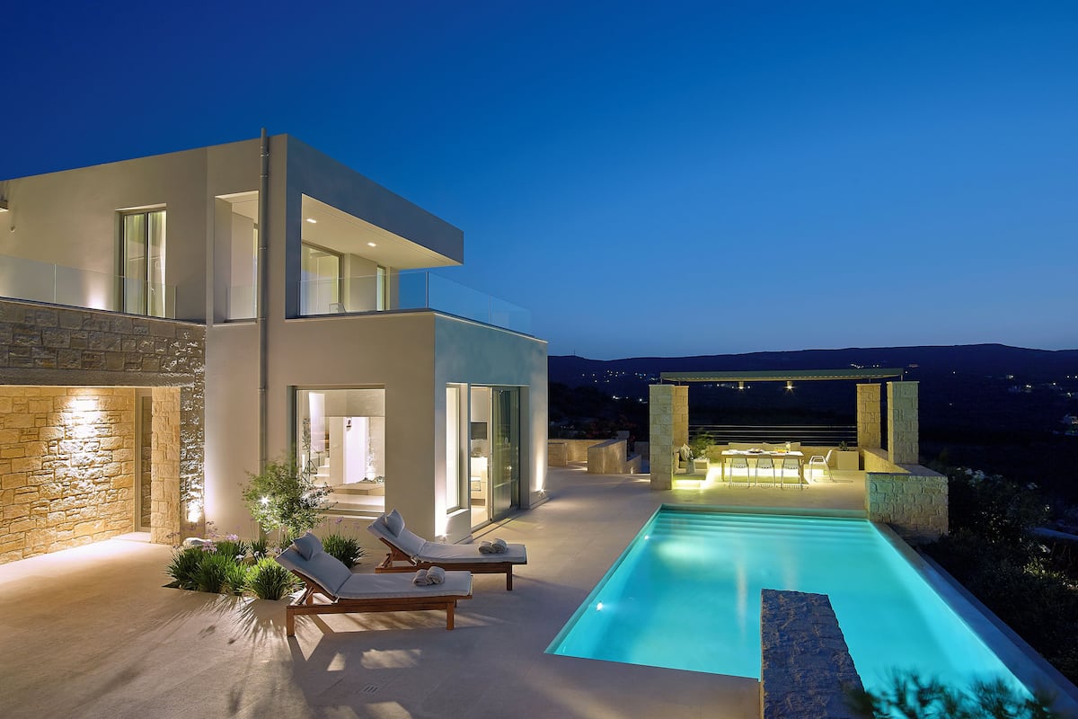 A modern house with a swimming pool, outdoor seating, and a stone facade.