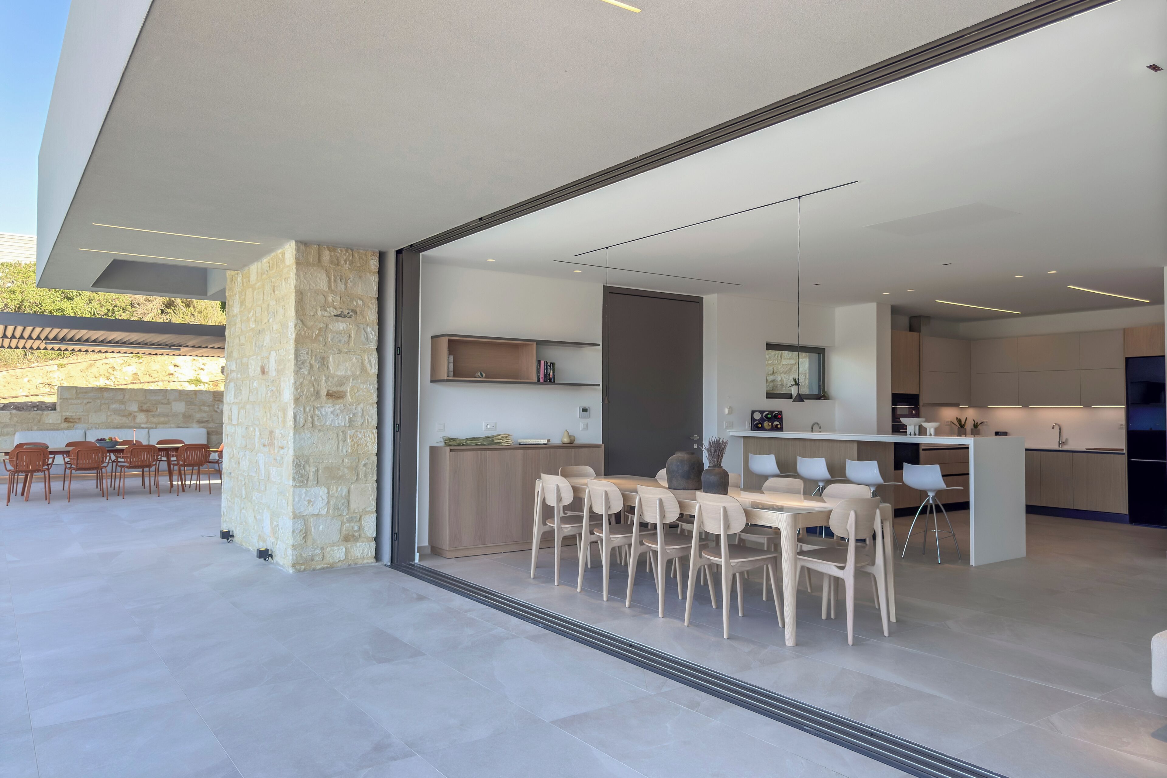 A modern kitchen with a central island, a dining area with chairs, and a stone pillar.