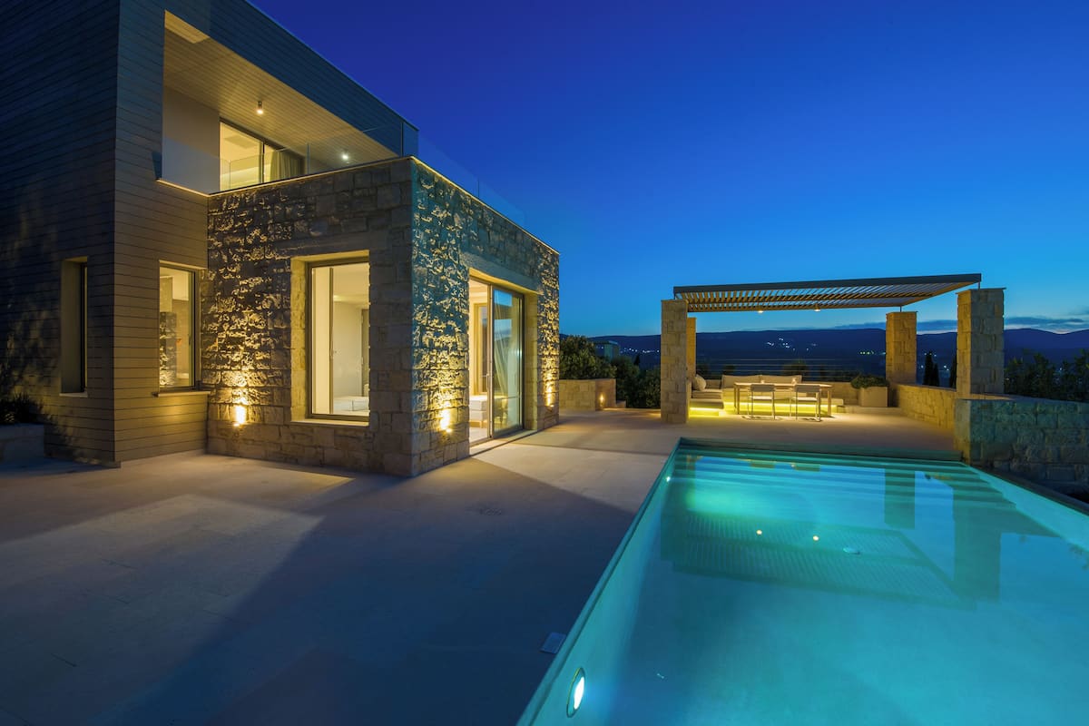 A modern house with a swimming pool, stone facade, and a pergola.