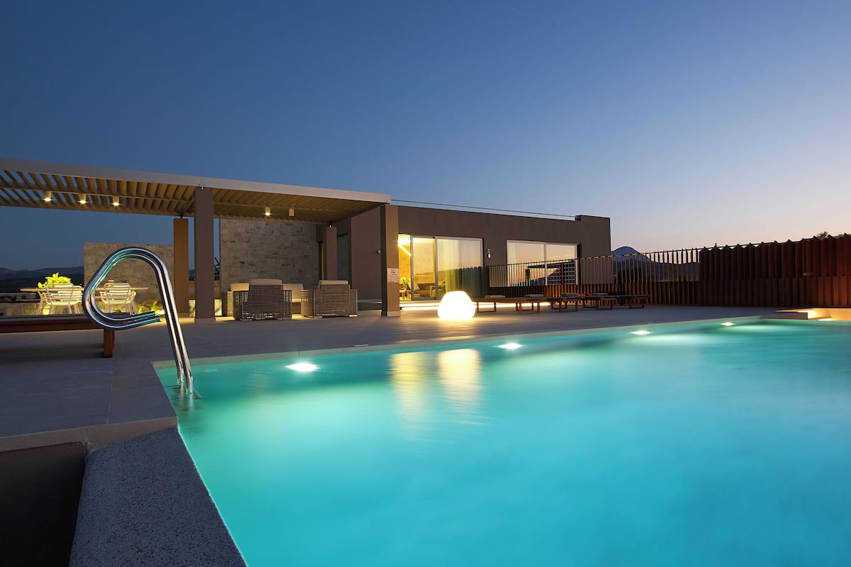 A modern outdoor pool area with lounge chairs, a pergola, and a view of the mountains.