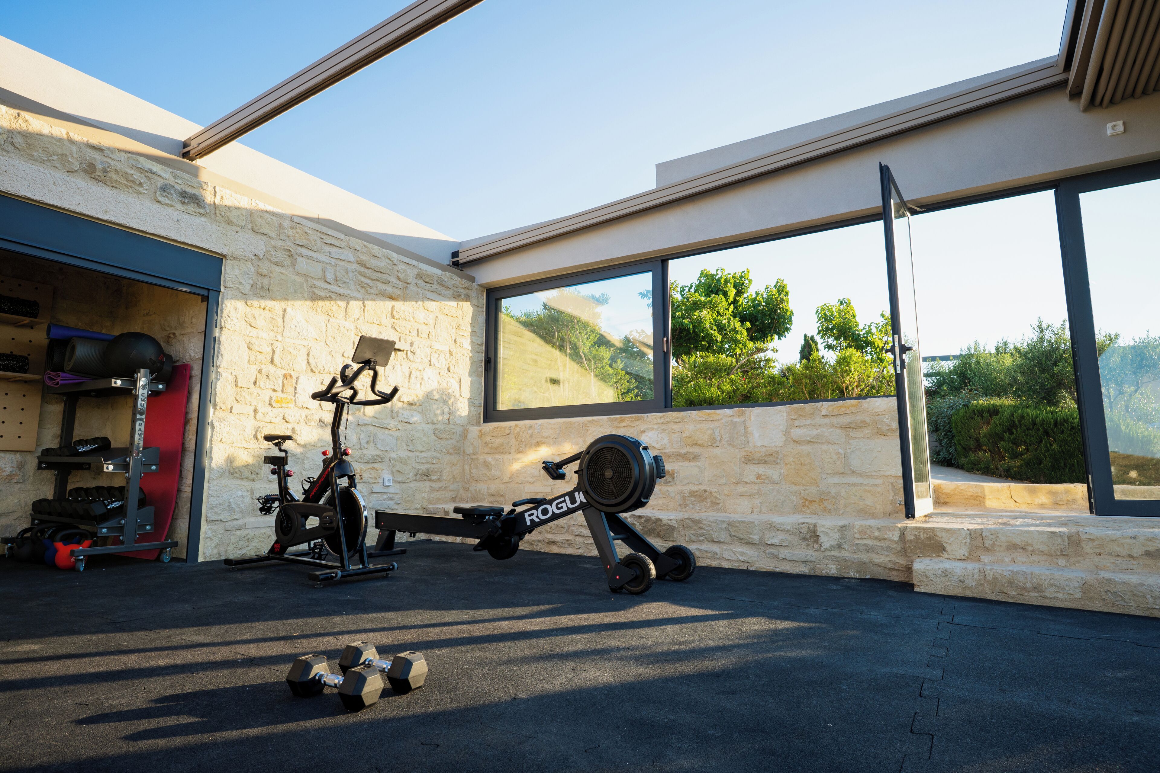 A home gym with exercise equipment, a stone wall, and large windows overlooking a green landscape.