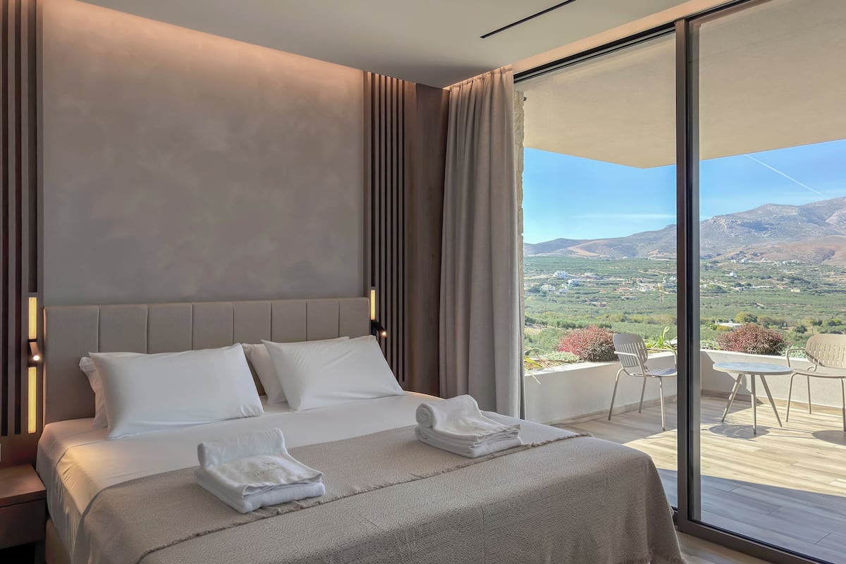 A hotel room with a bed, a view of the outdoors, and a balcony with chairs.