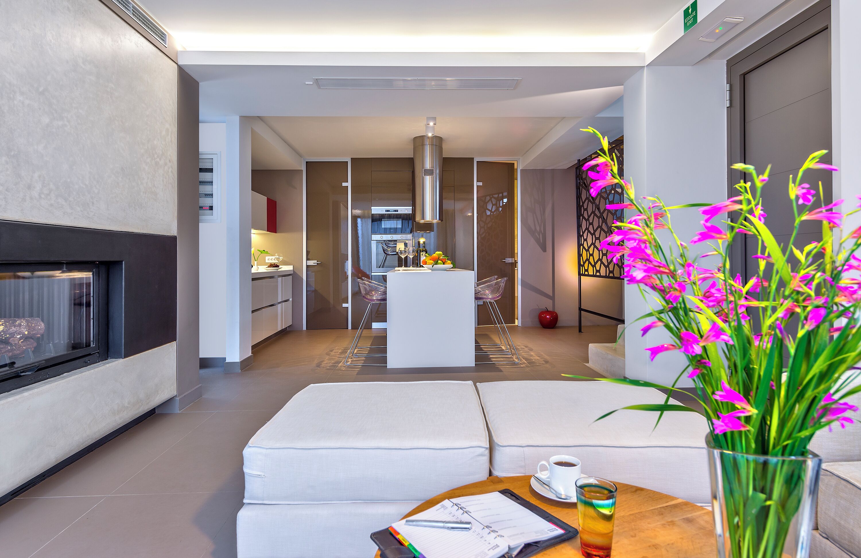 Una sala de estar moderna con chimenea, un comedor con isla central y una cocina al fondo.