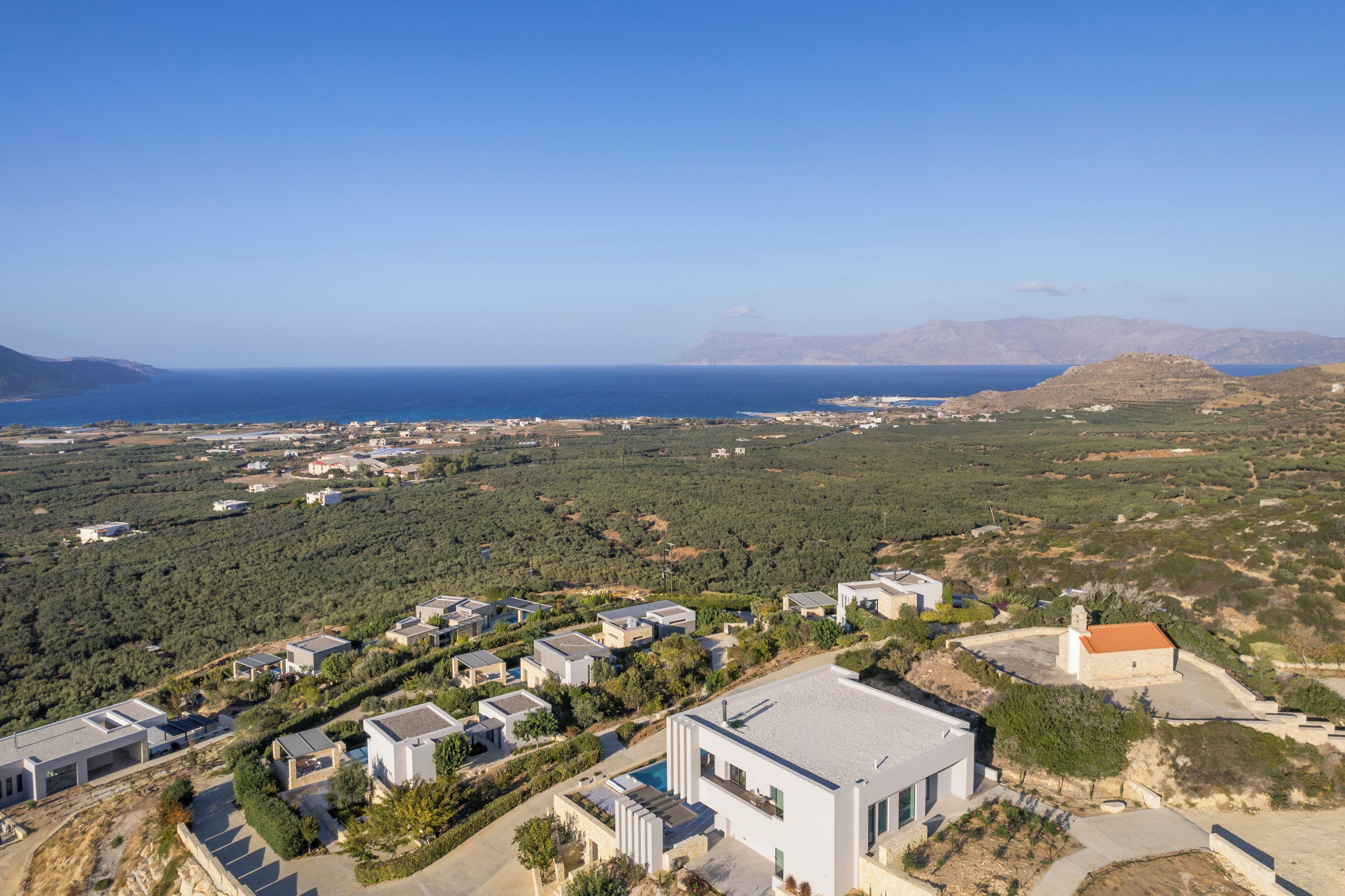 A coastal residential area with modern houses, a small church, and a clear view of the sea.