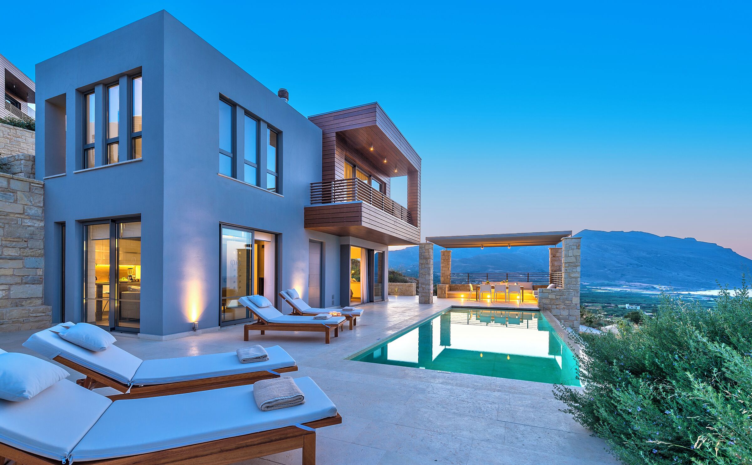 Una casa moderna con piscina, sillones de descanso y vistas a las montañas.