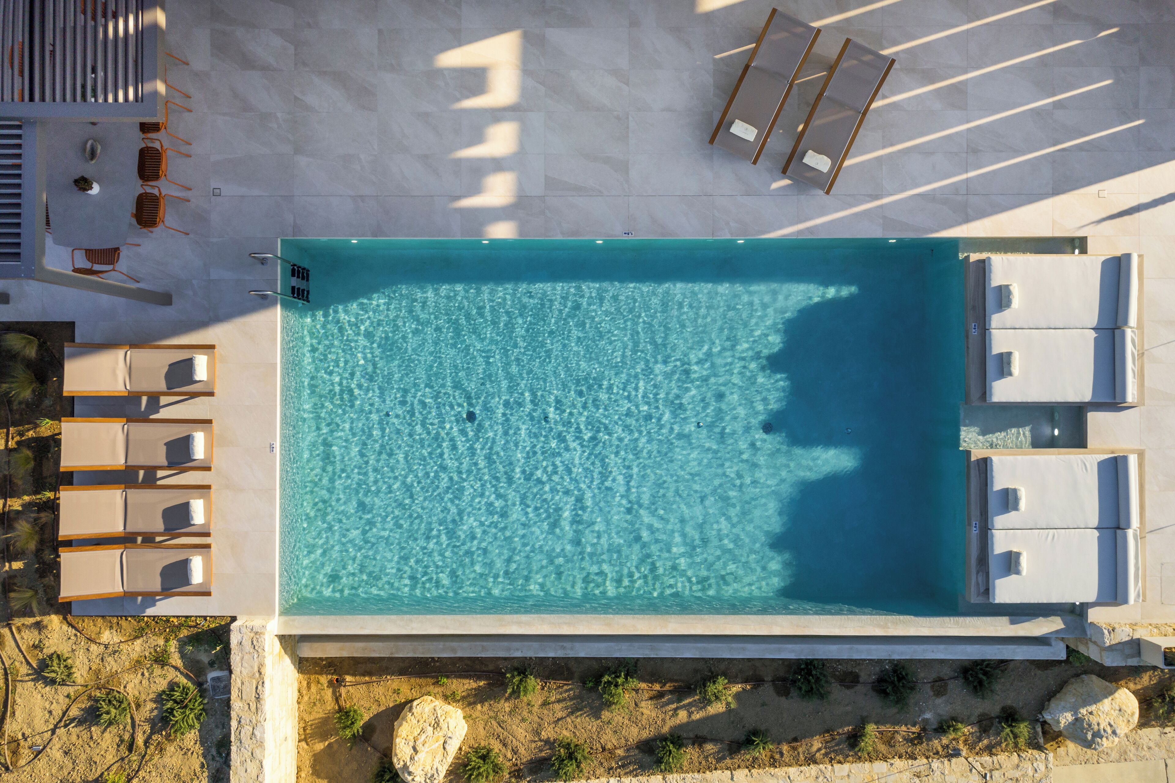 Une vue aérienne d’une piscine rectangulaire à l’eau d’un bleu limpide, entourée de chaises longues et de transats.