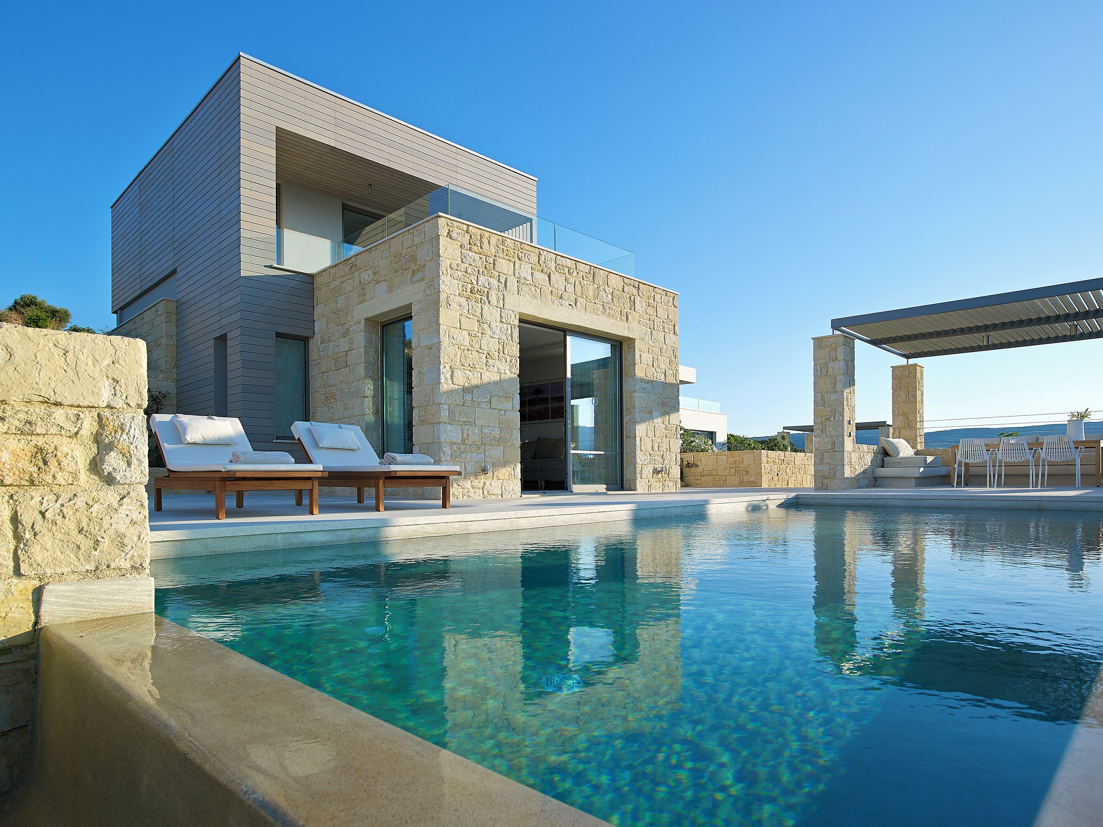 Una casa moderna con piscina, muros de piedra y mobiliario para exteriores.