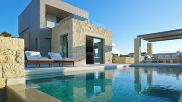 Una casa moderna con piscina, muros de piedra y mobiliario para exteriores.