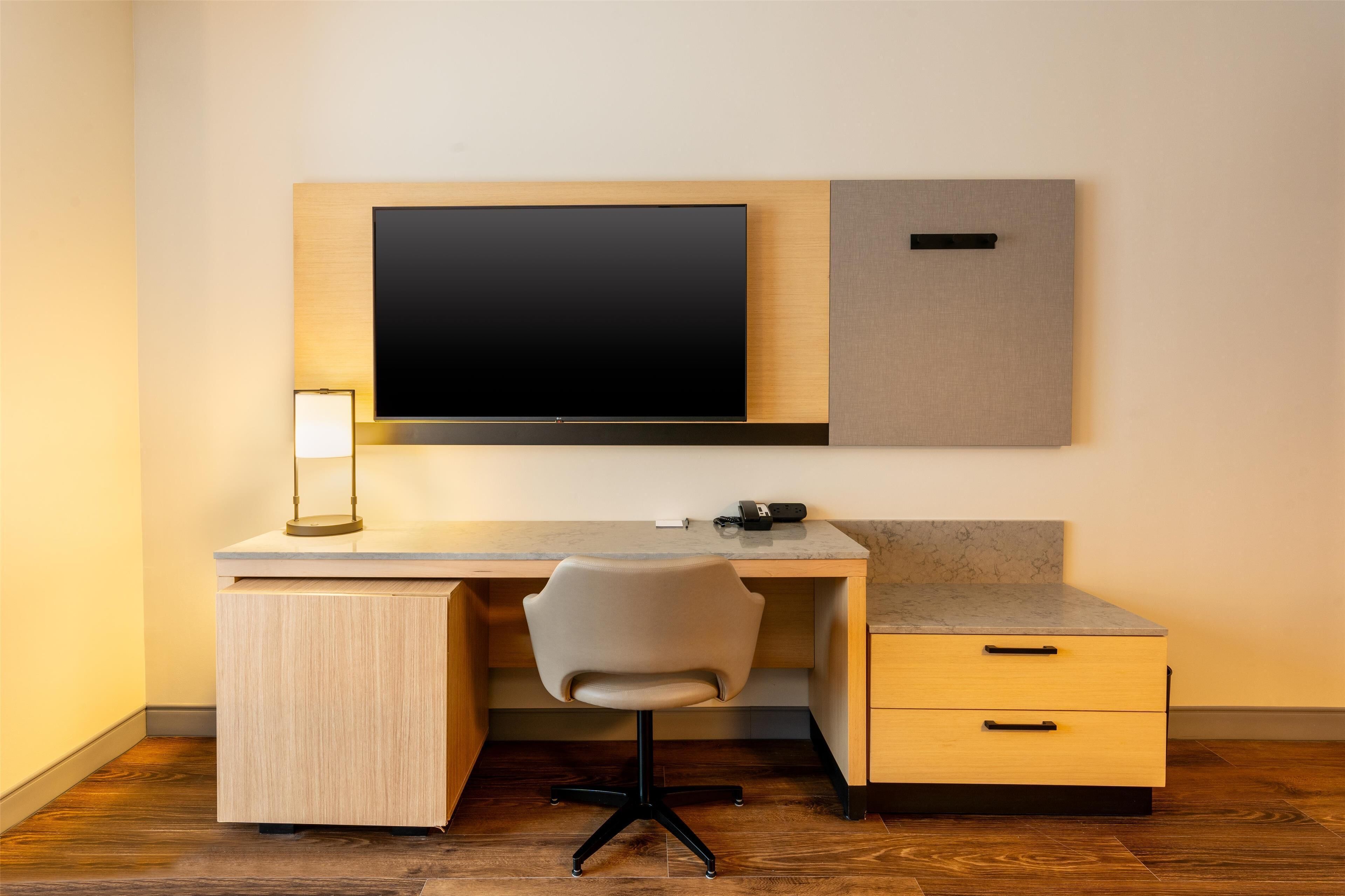 Een modern bureau met een flatscreen televisie, een lamp, een stoel en een klein dressoir.