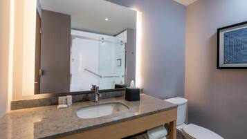 A modern bathroom with a marble sink, a large mirror, a framed artwork, and a visible shower area.