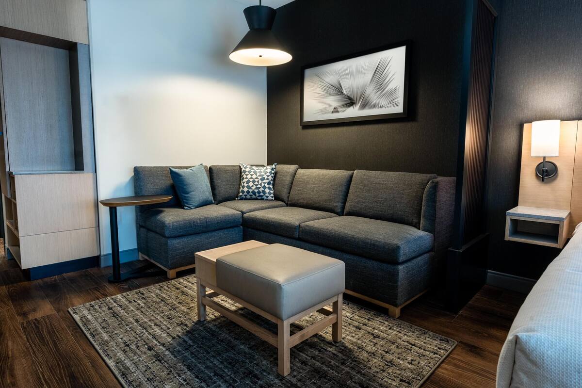 Un salon moderne avec un canapé d’angle, une petite table d’appoint, un banc en bois et une lampe sur pied.