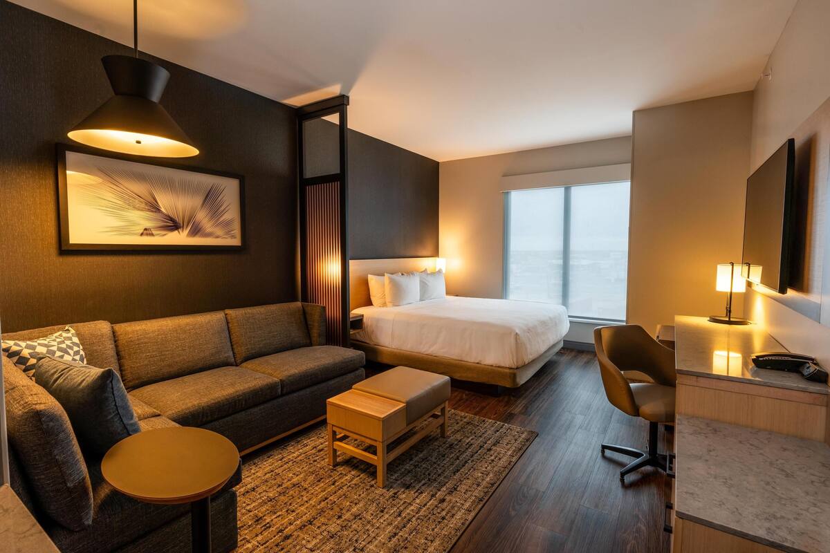 Une chambre d’hôtel moderne équipée d’un canapé, d’un lit, d’un bureau et d’une grande fenêtre.