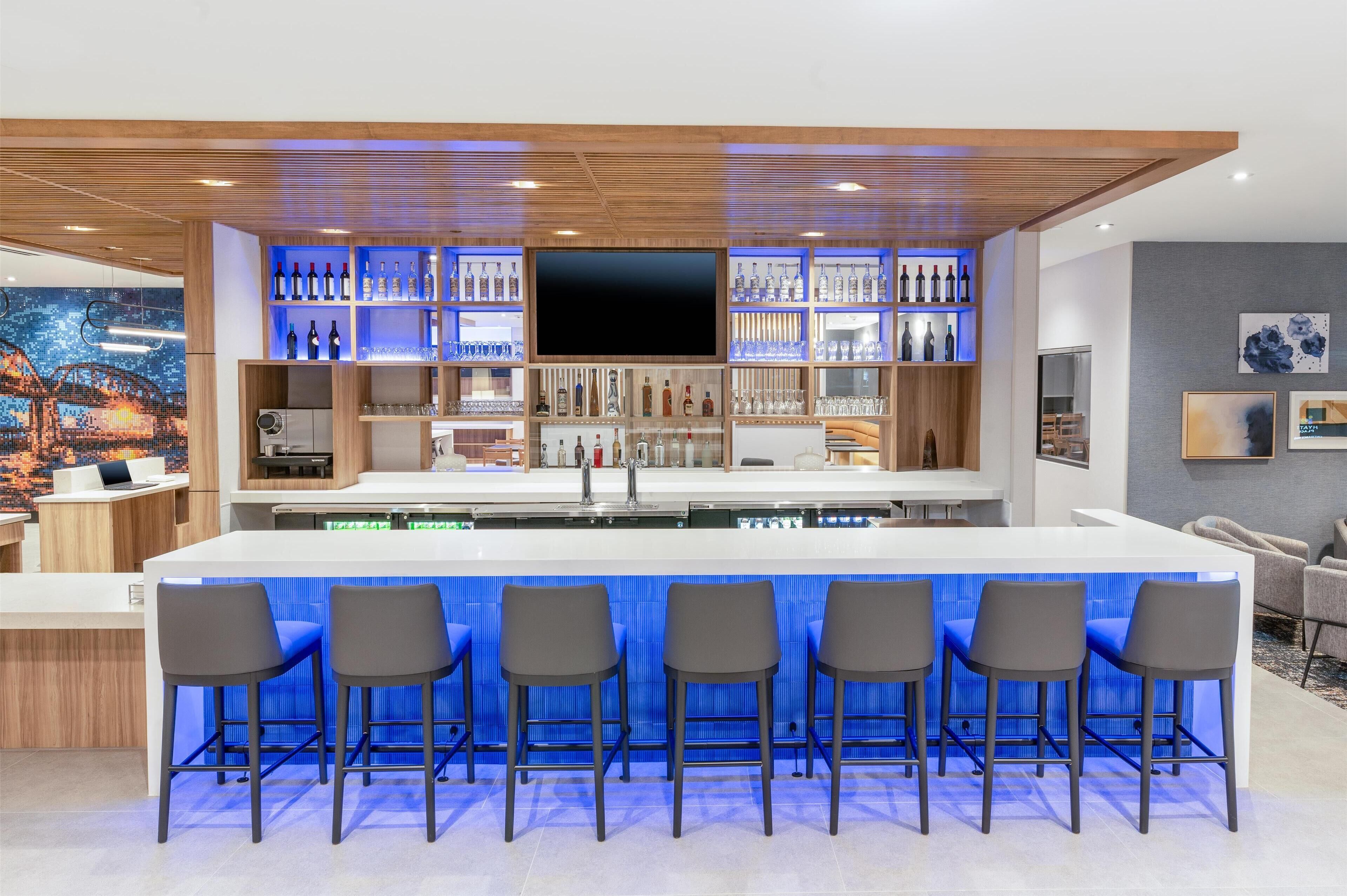 A modern kitchen with a central island, bar area with stools, and a large TV.