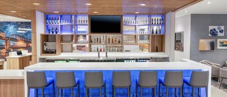 A modern kitchen with a central island, bar area with stools, and a large TV.