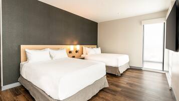 A hotel room with two beds, a dark accent wall, a wooden floor, and a large window.