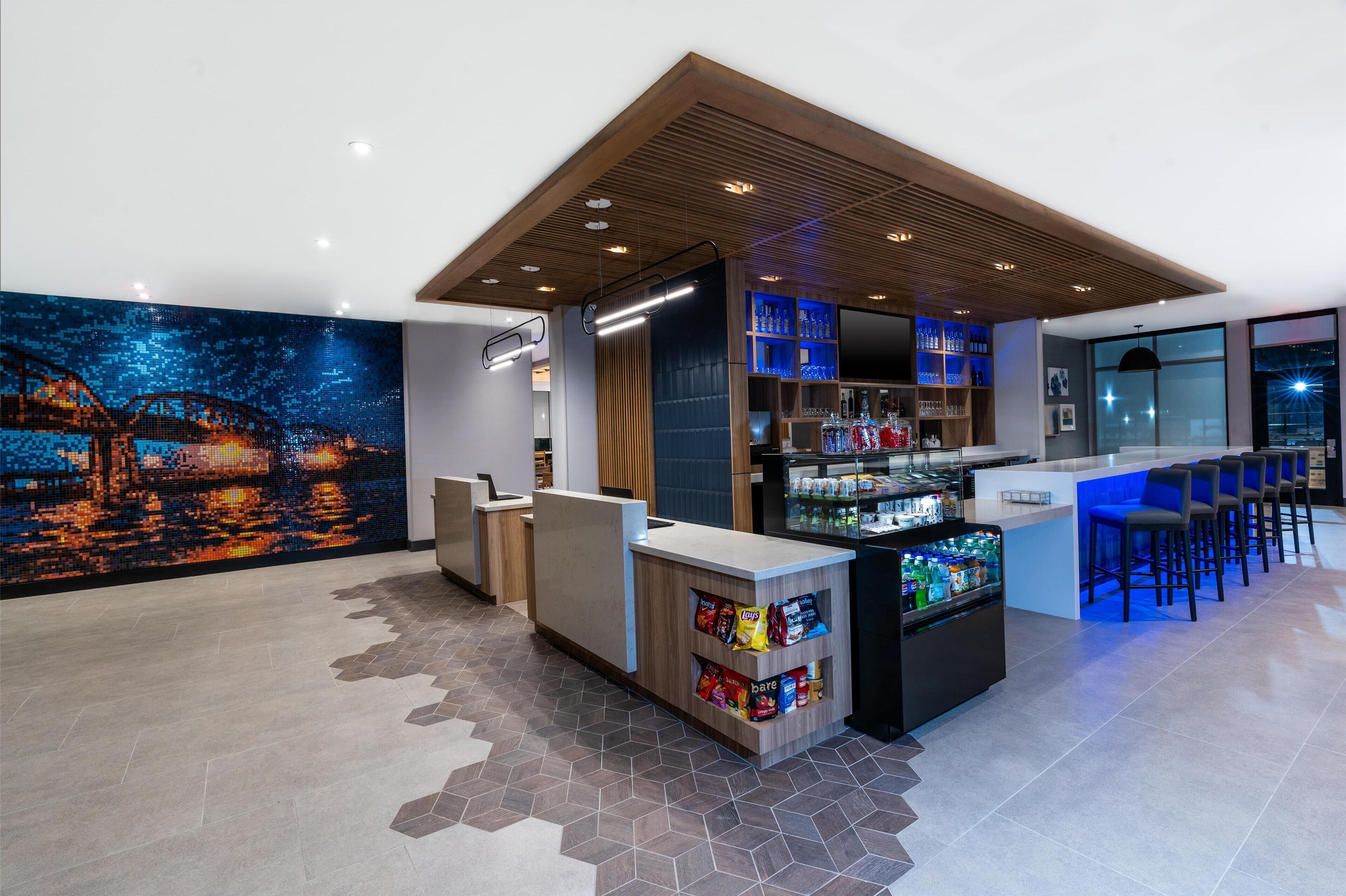A modern bar area with a cityscape mural, a counter with snacks, and a seating area with bar stools.