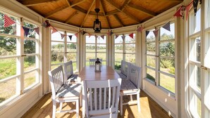 Eine überdachte Terrasse mit Holzbalkendecke, weißen Fensterrahmen und einem Tisch mit Stühlen.