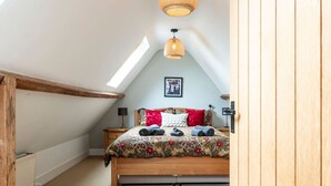 Ein Schlafzimmer mit schrägen Wänden, einem hölzernen Bett, einer roten und weißen Bettdecke, einer hängenden Leuchte und einem gerahmten Bild an der Wand.