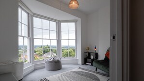 A room with large windows, a green sofa, a white rug, and a hanging light fixture. - Cosy 1BD in Malvern With Stunning Views (Malvern)