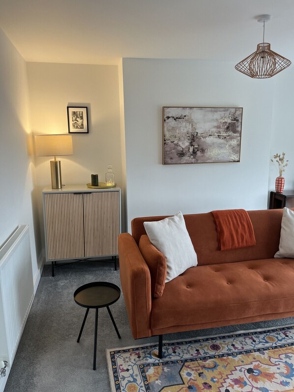 A modern living room with a brown sofa, a small round table, a lamp, a radiator, and a colorful rug.